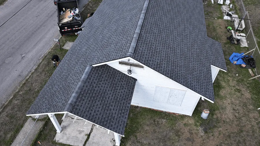 Aerial view of a fresh dark shingle roof with tear-off cleanup underway